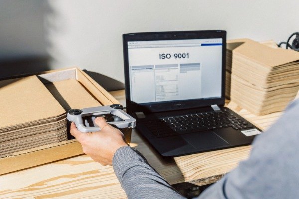 ISO verification Person holding drone near laptop showing ISO 9001 document (ID#3)