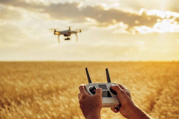 Person controlling a drone over a golden field at sunset (ID#2)