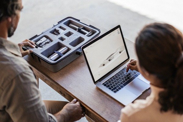 Two people reviewing drone designs on a laptop with drone parts (ID#5)