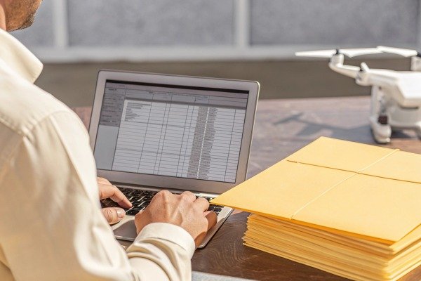 Person working on laptop with drone and files nearby (ID#4)