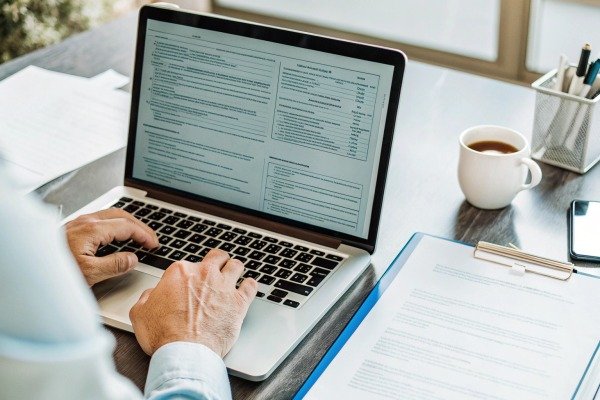 Person typing on laptop with documents and coffee (ID#5)