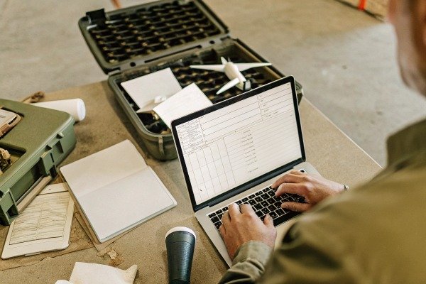 Person typing on laptop with drone equipment nearby (ID#5)