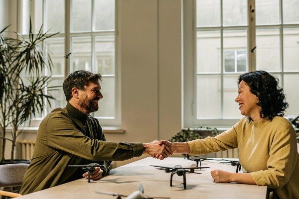 Two people shaking hands with drones on table (ID#5)