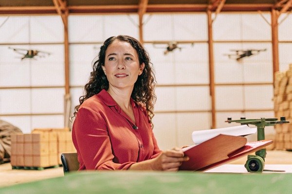 Woman reviewing documents in warehouse with drones (ID#5)