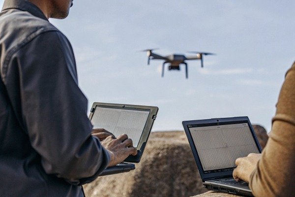 People using laptops controlling drone outdoors (ID#4)