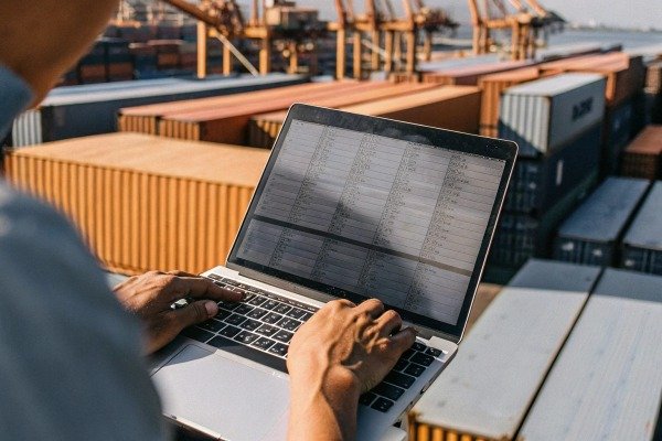 Person using laptop near shipping containers (ID#2)