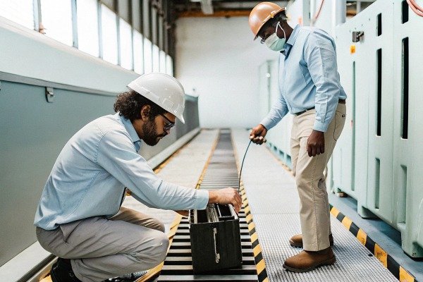 Two technicians in safety gear inspecting industrial equipment on a conveyor line (ID#3)