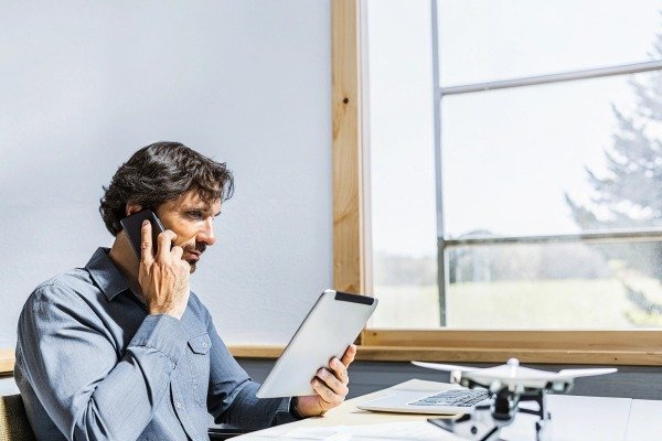 Drone Pilot Business Call Professional man talking on phone while reviewing data on a tablet near a drone (ID#5)