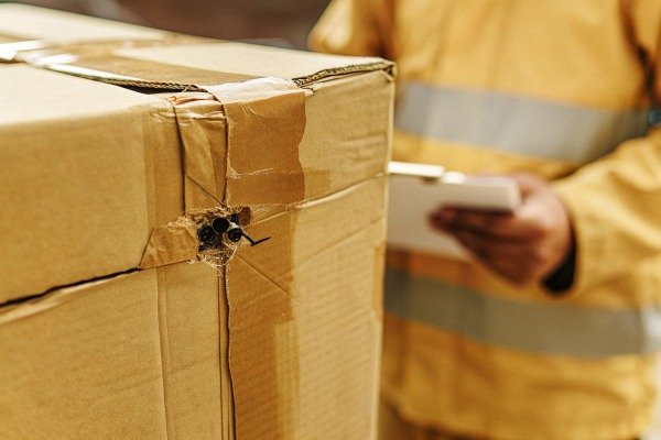 Close-up of a damaged cardboard box showing a hole from shipping mishandling (ID#4)
