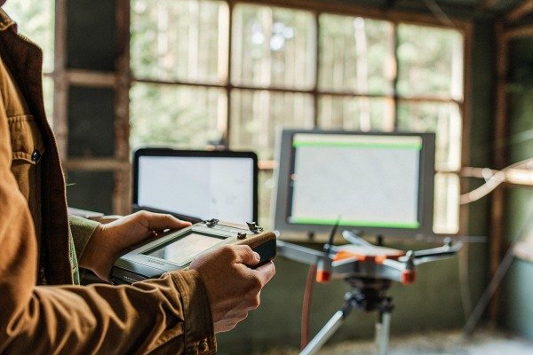 Person holding a professional drone remote controller with a screen in a workshop (ID#3)