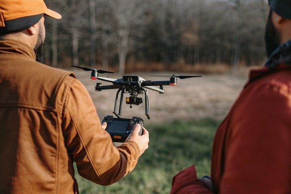 Drone pilot operating a professional quadcopter with a remote controller in a field (ID#4)
