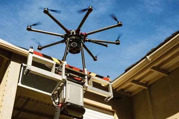 Large industrial multi-rotor drone carrying heavy sensor equipment near a building (ID#3)