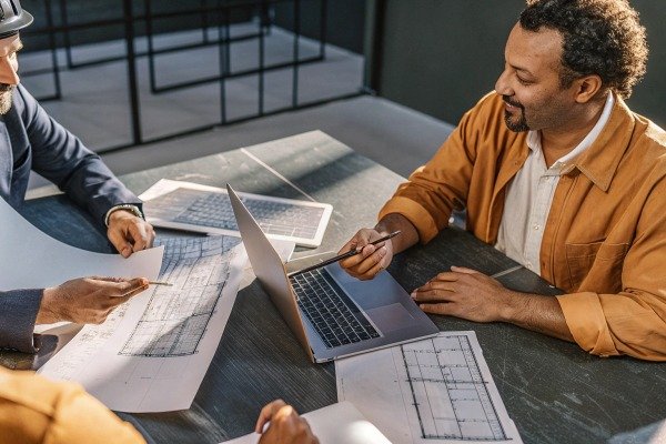 Engineers discussing architectural blueprints and project details on a laptop in an office (ID#2)