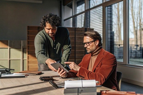 Two professional men discussing data on a digital tablet in a bright modern office (ID#5)
