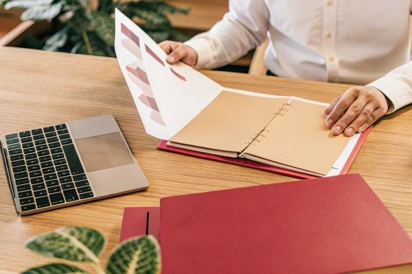 A person reviewing data charts and documents next to a laptop on a desk (ID#3)