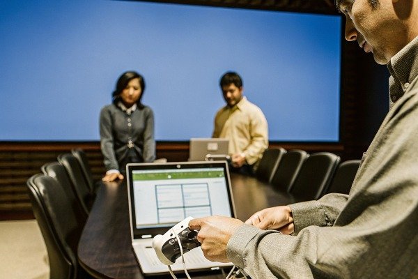 Man operating a drone controller in front of a laptop in a meeting room (ID#2)
