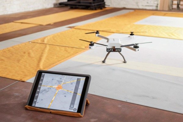 White quadcopter drone on a workshop floor with a tablet displaying flight map data (ID#5)