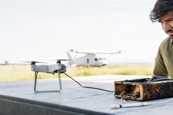 Technician inspecting a small drone connected to a portable power source outdoors (ID#5)