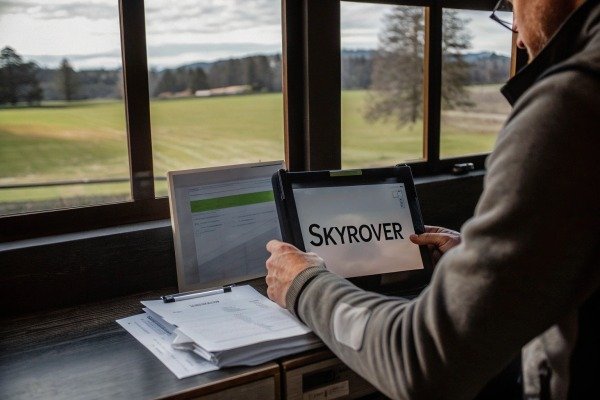 Person holding a tablet displaying SkyRover software while overlooking a rural field (ID#5)