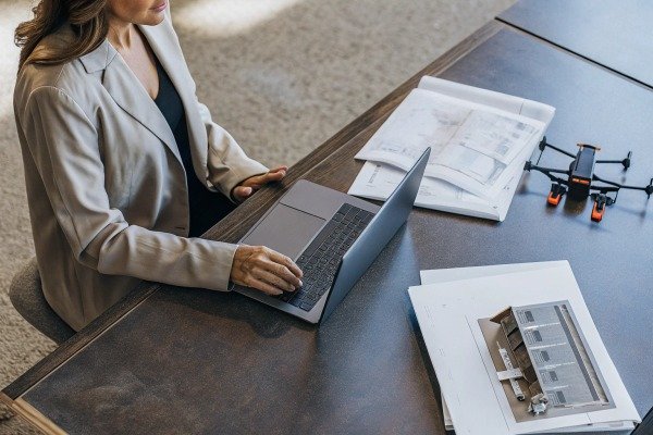 Businesswoman working on a laptop next to architectural drawings and a drone (ID#5)